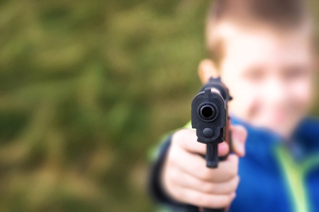 Young boy,holding a toy gun,against green grass background.の写真素材
