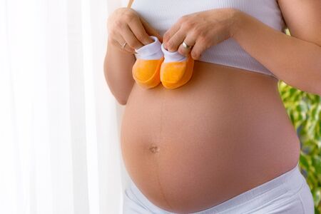 Pregnancy concept. Young pregnant woman holding baby shoes on her belly.の写真素材