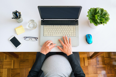 Pregnant business woman sitting at the desk and working on the laptop. Top view.の写真素材