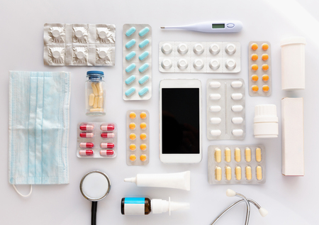 Various medications and medical equipment with smart phone in the center, laid flat on top of white board.の写真素材