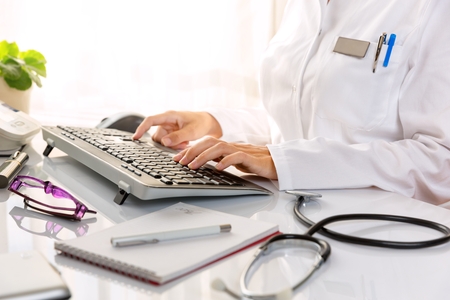 Close up of a female doctor, typing on the desktop computer.の写真素材