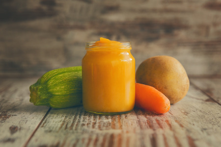 Homemade baby food in jar, next to raw vegetables.の写真素材
