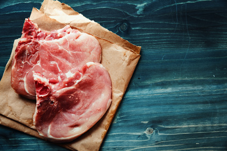 Raw pork chops on top of the blue wooden background.