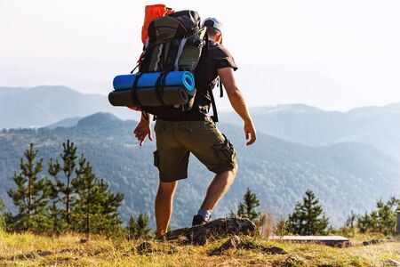 Male backpacker trekking through the mountains, with mountain peaks visible in the distance.の写真素材