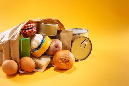 Various groceries inside paper bag on top of yellow background, with available copy space. Stockpiling food concept.の写真素材