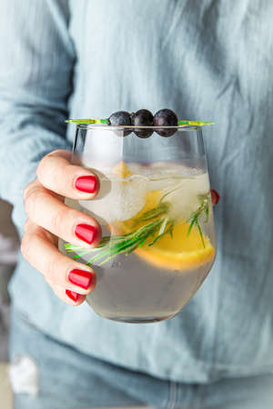 Close up of a woman hand holding fresh  lemonade. Blueberry, lemon and organic herb in ice cold glass.の写真素材