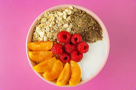 Healthy breakfast with yogurt, cereal, and ripe fruit served in bowl. Isolated on pink background.