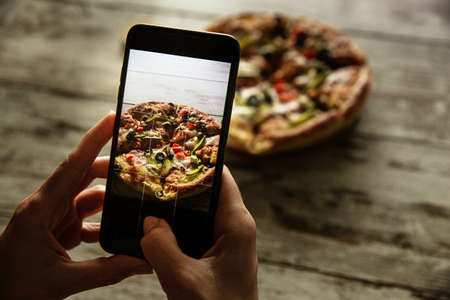 Female hands holding a smartphone and taking photo of a delivered pizza.の写真素材