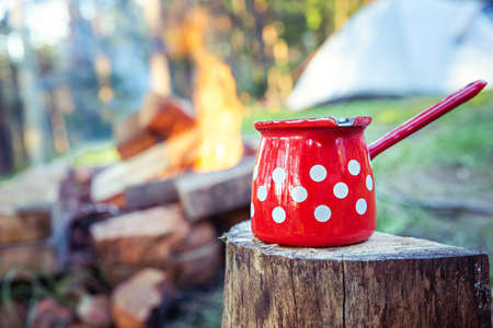 Close up of red coffee pot, in front of campfire, with sleeping tent in background.の写真素材