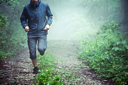 Close up of male athlete, wearing outdoor clothes, running through misty forest early in the morning. Copy space available.の写真素材