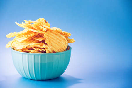 Ribbed potato chips inside the bowl, isolated against blue background, with copy space next to it.の写真素材