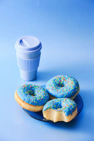 Served donuts with blue icing in a blue plate, with blue coffee mug next to it, isolated on top of blue background.の写真素材