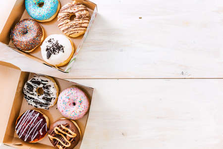 Colorful donuts with various icing on top of them, inside take away boxes, with negative space next to them.の写真素材