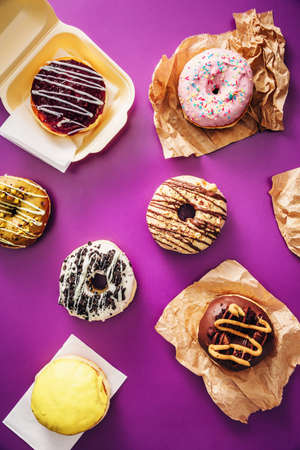Group of various colorful chocolate donuts, on top of purple background. High angle view.の写真素材