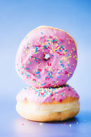 Two homemade donuts with pink glaze, isolated on light blue background.の写真素材