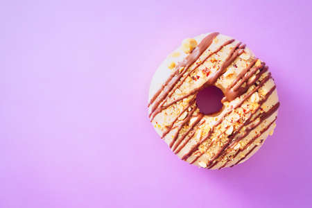 Close up of white chocolate donut with nuts, on top of purple background, with available negative space. Top down view.の写真素材