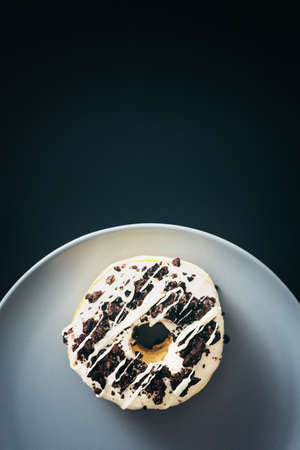 Close up of white chocolate donut with crushed chocolate cookie on top of it, served in gray plate with negative space next to it.の写真素材
