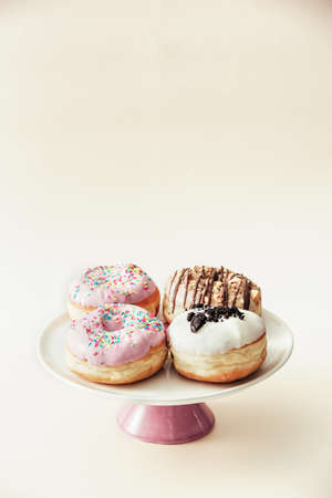 Group of different chocolate donuts served on top of dessert plate, isolated against pale beige background, with copy space available above it.の写真素材