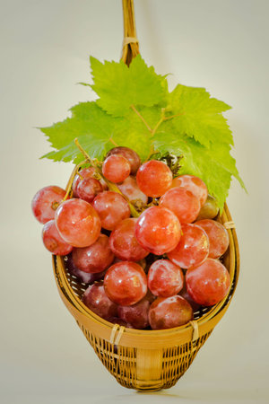 red grape with leaves in colander made from bamboo on white background.の写真素材