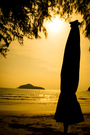 Tropical beach and umbrellas silhouettes in sunset lightの写真素材