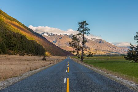 asphalt road through the field with mountain at the backgroundの写真素材