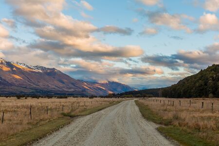 gravel road through the field with mountain at the backgroundの写真素材