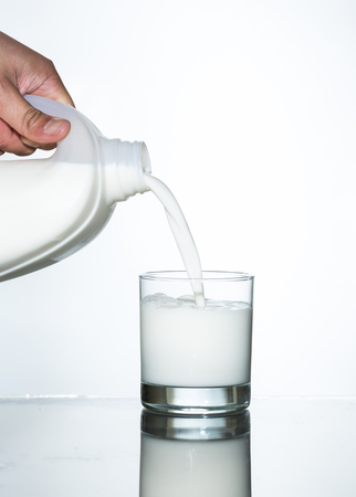 pouring milk into glass on white backgroundの写真素材