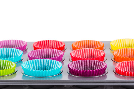 muffins baking tray with colourful paper cases isolated on white