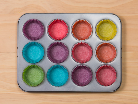 muffins baking tray with colourful paper cases on wooden background