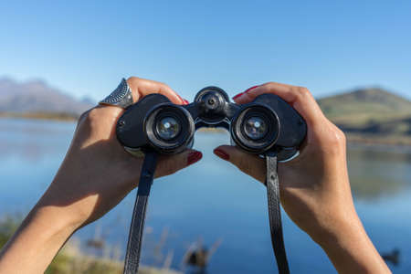 hands holding binoculars point to Lake Hayes in New Zealandの写真素材