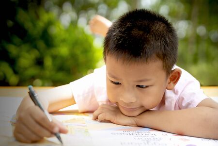 Elementary age boy writing in book while lying down on floor.A boy lie down writing in a book.の写真素材