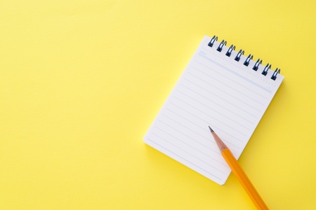 Notepad and orange technical pencil on yellow backgroundの写真素材