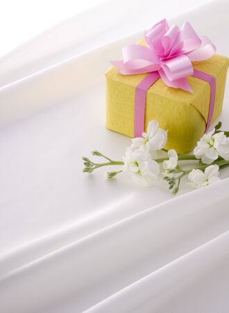 yellow gift box with pink ribbon on white satinの写真素材