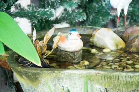 Little figurine of a bird sitting on a stone in the water