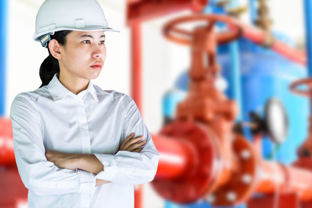 Confident female engineer standing with arms crossed against pipeline in boiler roomの写真素材
