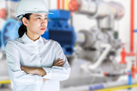 Portrait of a female engineer standing with arms crossed against blue industrial backgroundの写真素材