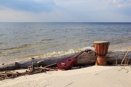 Ukulele and ethnic drum on a sunny beach over sky background.の写真素材