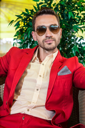 Handsome adult model wearing red jacket and fashionable sunglasses. tree on the backgroundの写真素材