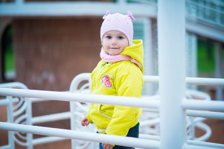 Funny baby girl in a yellow coat and pink hat and knitted scarf playing in a beautiful parkの写真素材