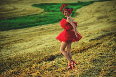 A young woman in a bright red dress with flowers in her hair in autumn field under the blue skyの写真素材