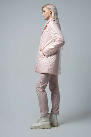 attractive woman in white coat and trousers looking at camera on grey backgroundの写真素材