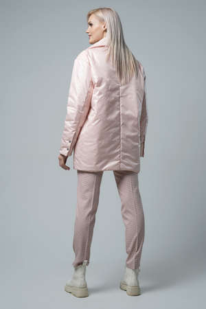 attractive woman in white coat and trousers looking at camera on grey backgroundの写真素材