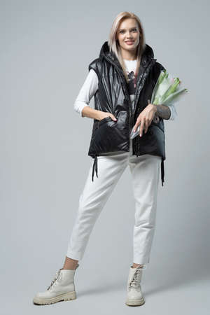 Blond young smiling happy woman in black vest with bouquet isolated on gray background studioの写真素材