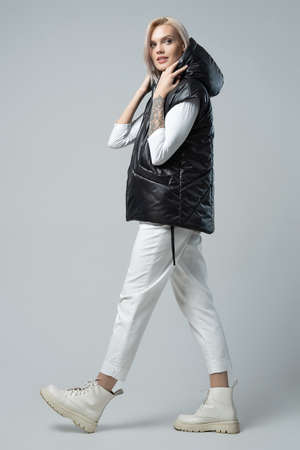 attractive woman in black vest and trousers looking at camera on grey backgroundの写真素材