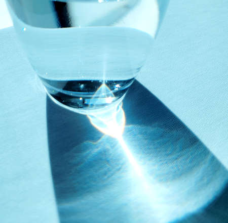 glass of water ,with blue reflection at the bottom of the glass on table, the blue color accentuate in different tonesの写真素材