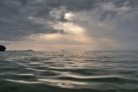 A wavy sea with city silhouette and gray cloudy skyの写真素材