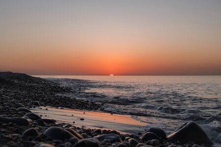 Sunset on the sandy and rocky beach with orange and lavender skyの写真素材