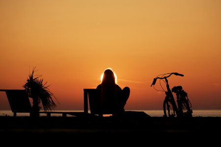 A girl with bike watching the sunset at the beachの写真素材