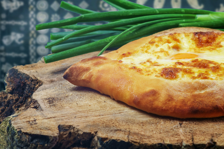 Adjarian khachapuri with egg and shallot on wooden tray with traditional tableclothe background,の写真素材