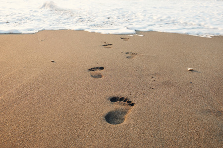 Footsteps in the sand to the foamy waveの写真素材